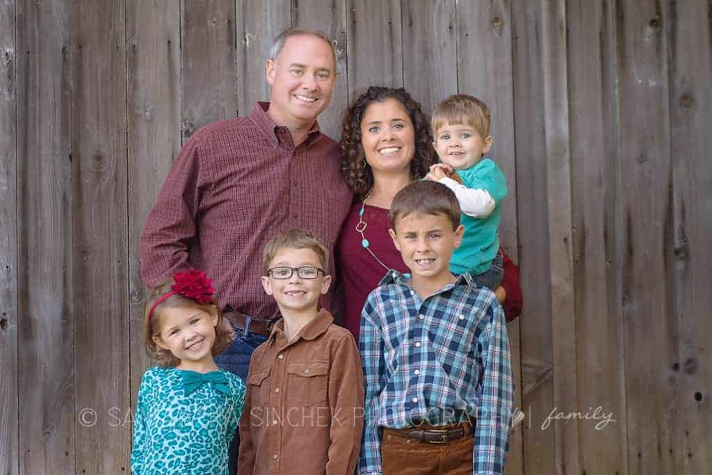 family of 6 stands against old barn wood during family photo session 