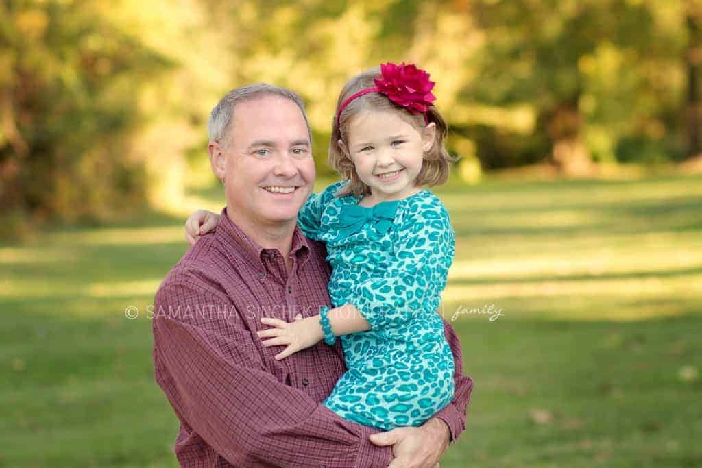 young girl smiles at camera in fathers arms