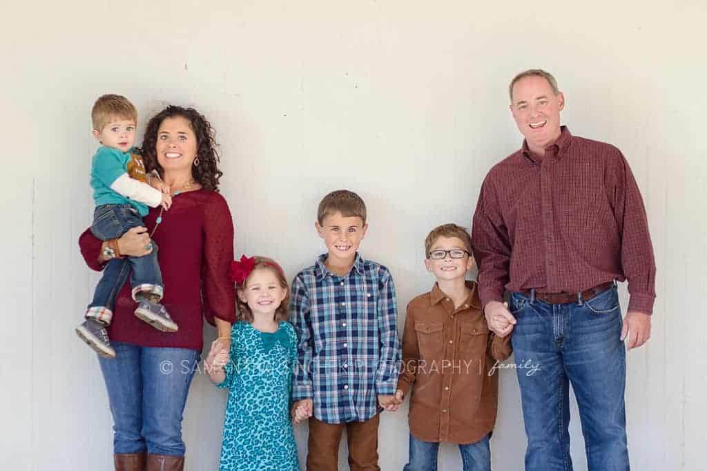 family of 6 stands against white barn