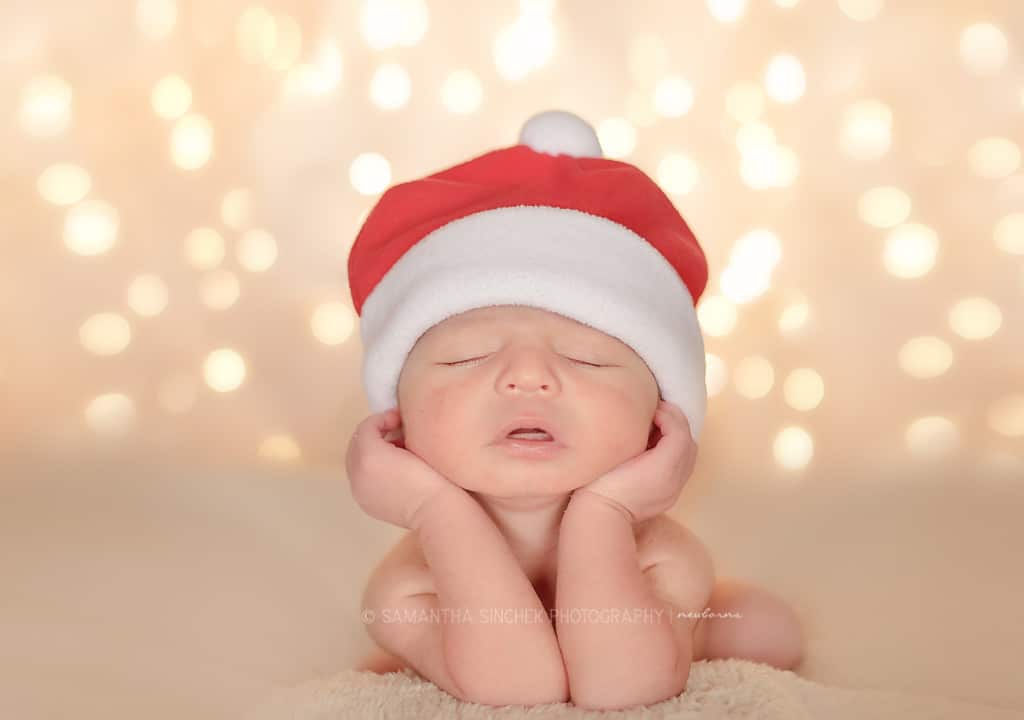 newborn boy wears santa hat in front of christmas lights