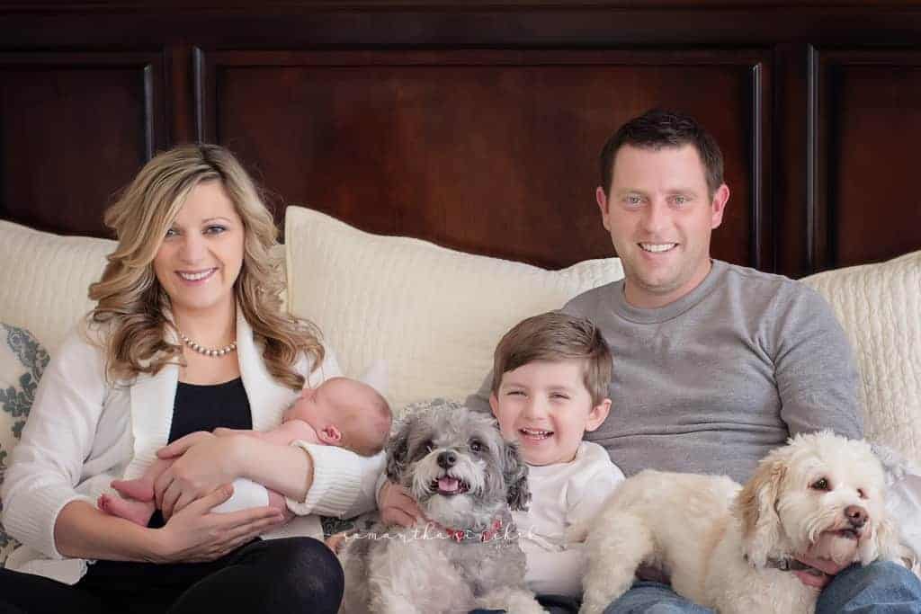family sits on bed with dogs newborn during pictures