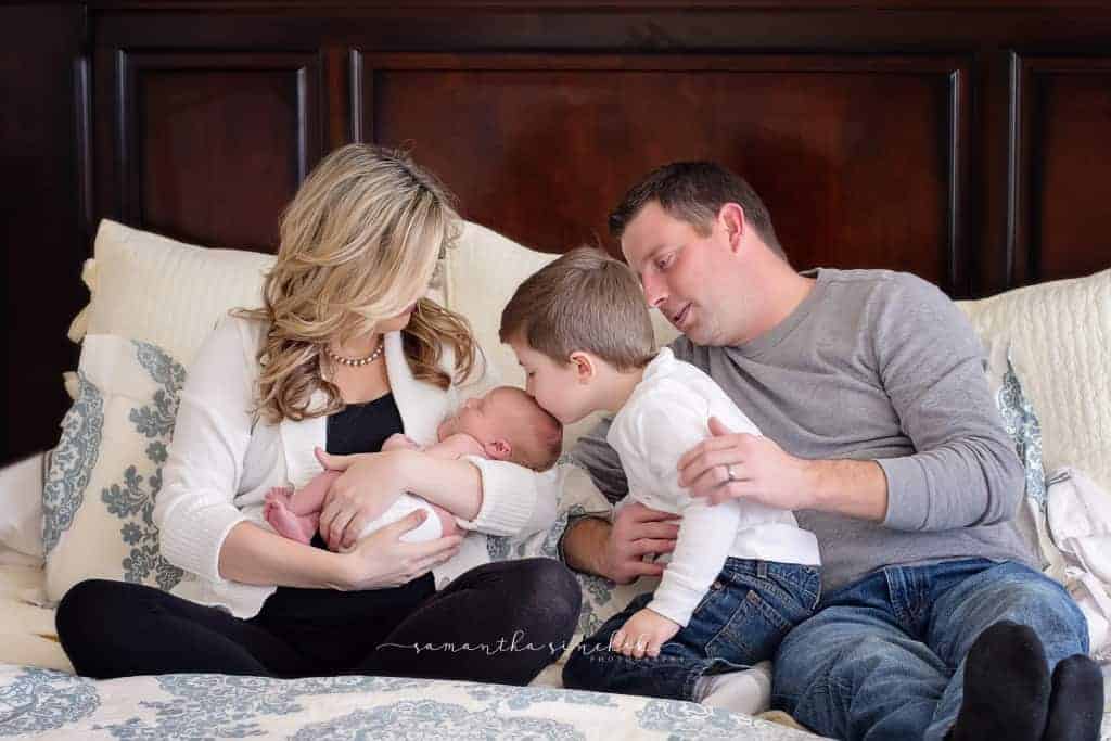 family sits on bed with dogs newborn during pictures