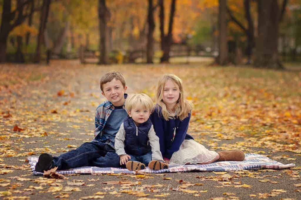three siblings sit on path at sharon woods during family pictures 