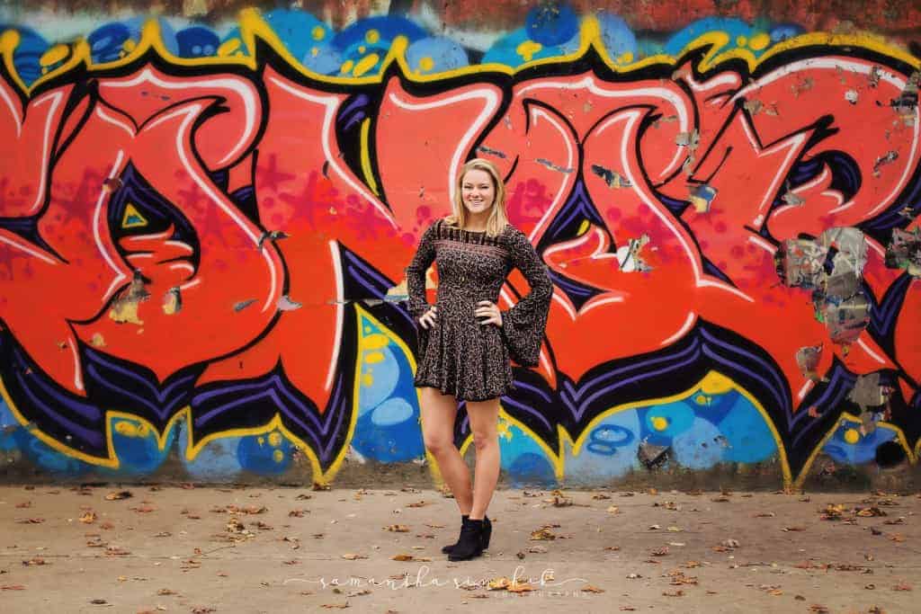 High school senior girl stands in front of graffiti wall