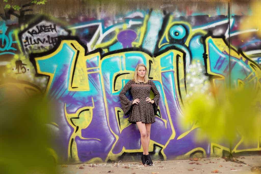 Senior girl in dress leans against graffiti wall in Cincinnati ohio
