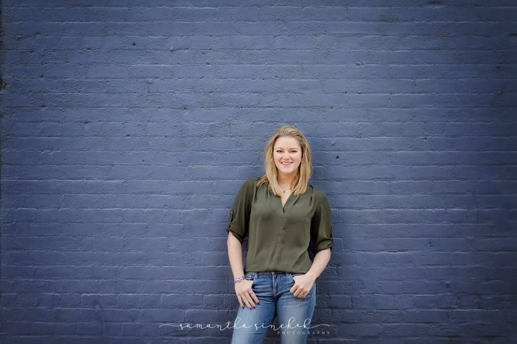 With fingers in her pockets a William mason high school senior stands against a blue brick wall
