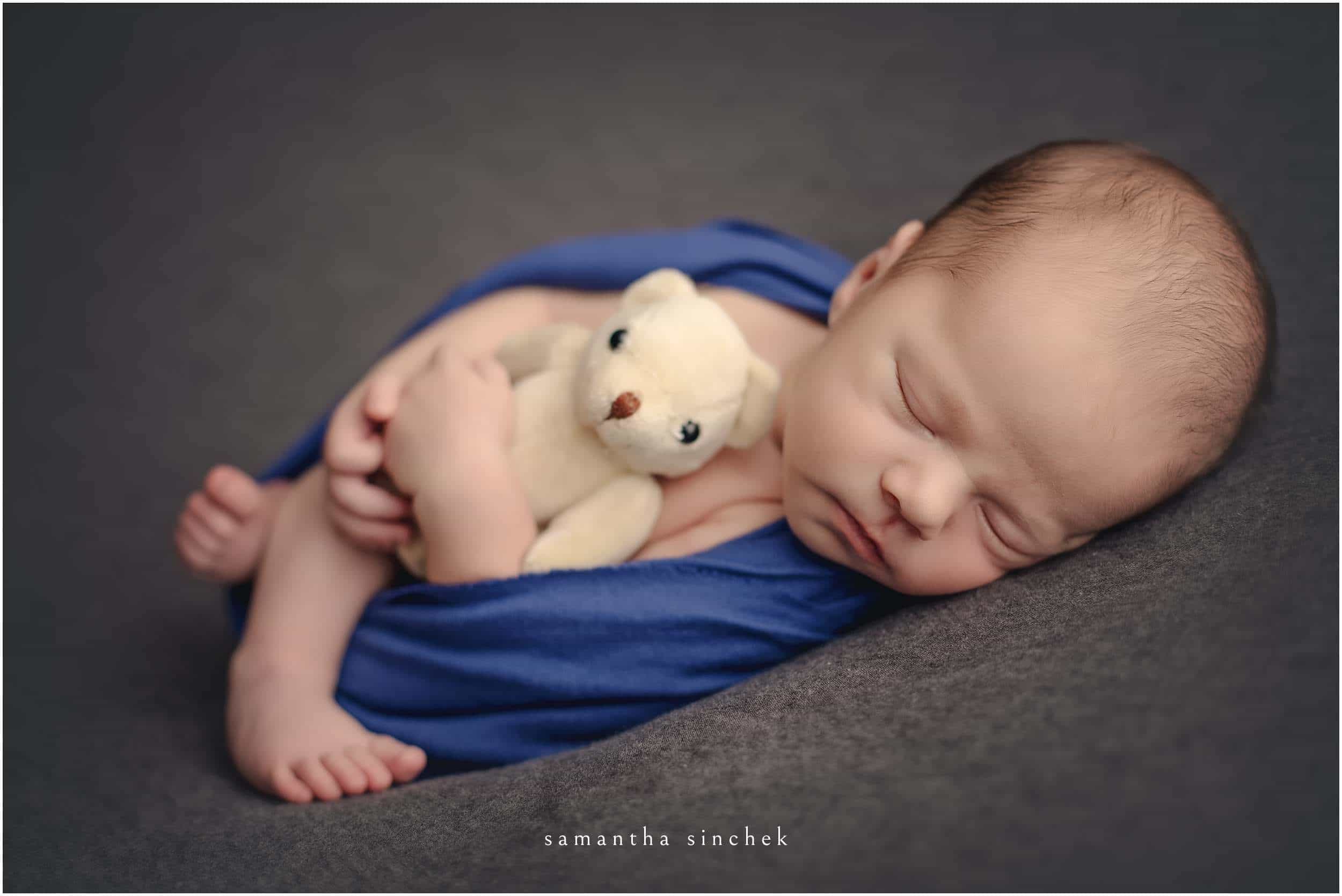 baby boy snuggles teddy bear at cincinnati newborn photographer studio