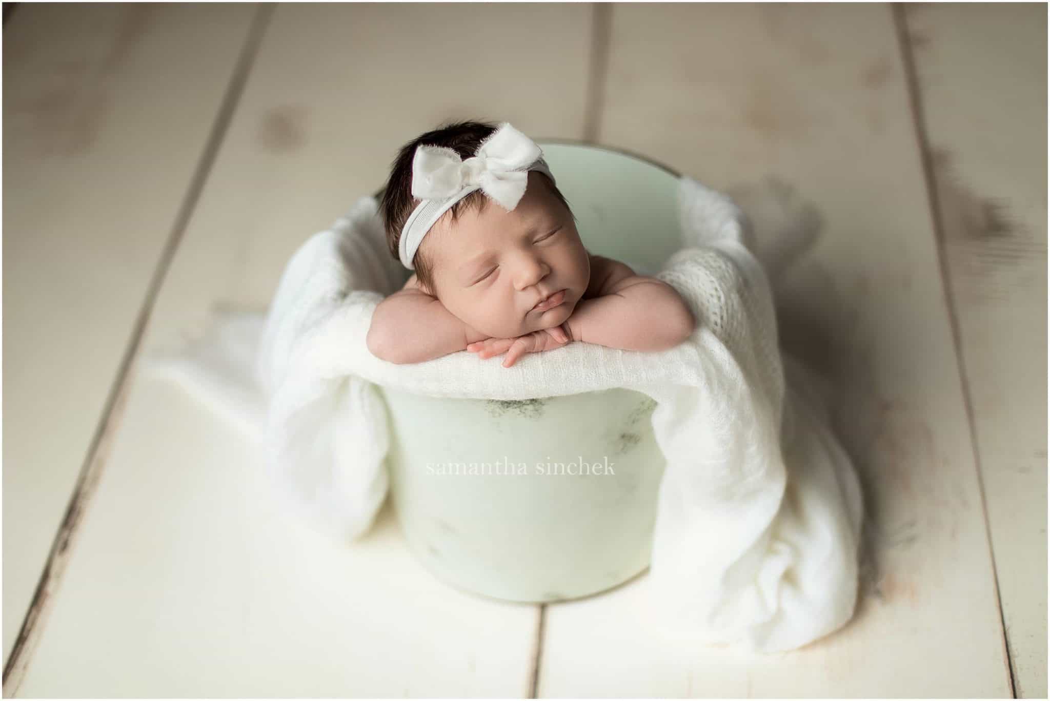 baby in a bucket with a white headband with cincinnati newborn photographer
