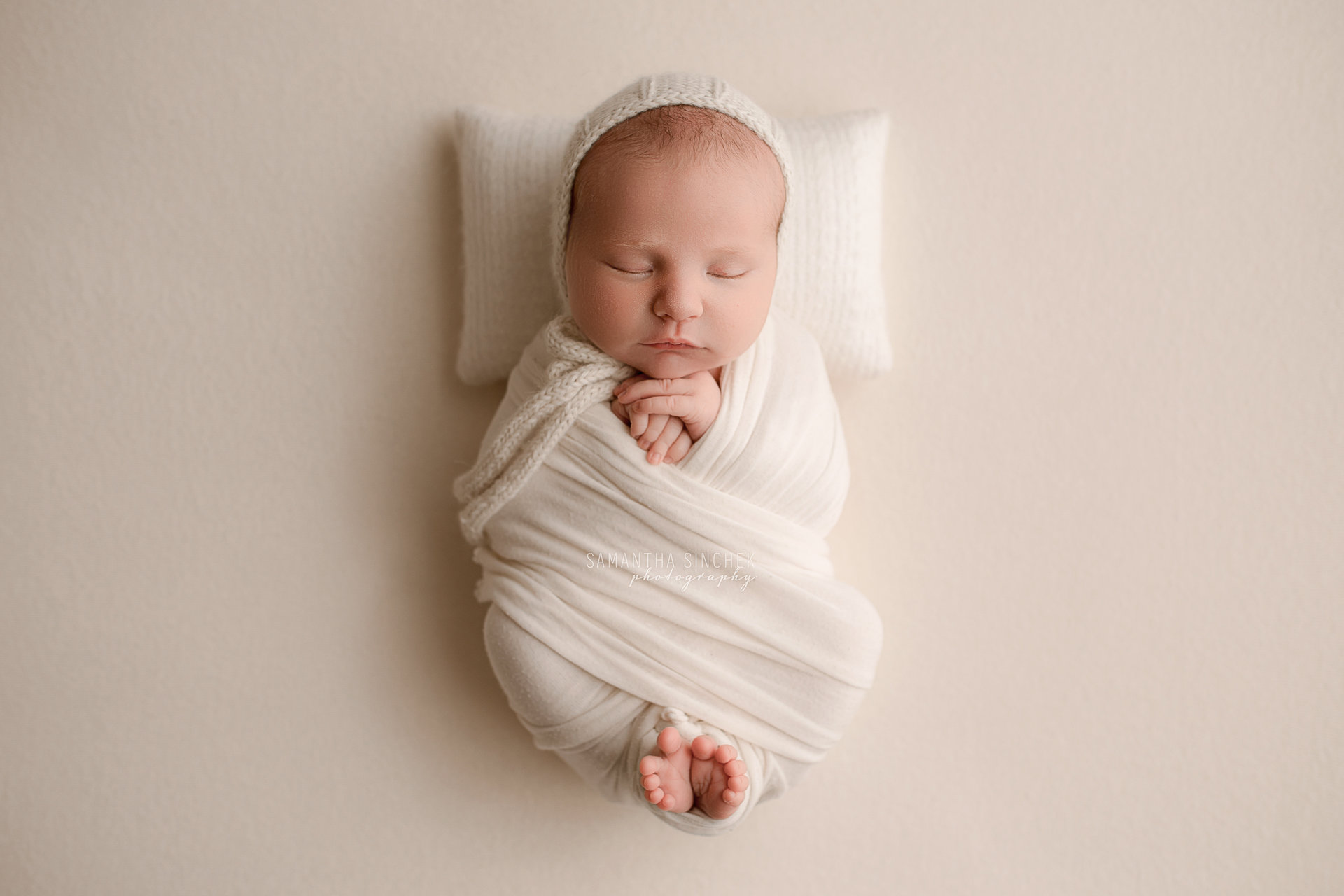 newborn sleeps with hands over her head on cream backdrop